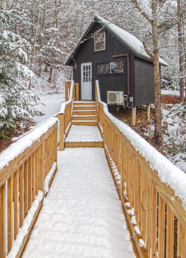 Una escalera de madera que conduce a una cabaña con una puerta y ventanas blancas, rodeada de árboles cubiertos de nieve.