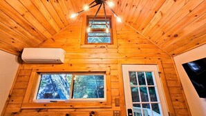 L’intérieur d’une cabane en bois, avec un plafond en pente, un luminaire central, deux fenêtres et une porte.