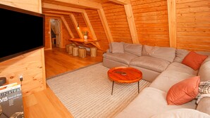 Une pièce confortable de style loft, avec un intérieur en bois, un canapé gris, une petite table basse en bois et un téléviseur à écran plat fixé au mur.