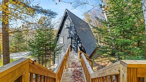 Un escalier en bois mène à un chalet dont le toit est sombre, entouré d’arbres et de feuilles d’automne.