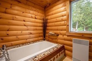 A log cabin bathroom with a bathtub, wooden walls, a window, and a small shelf with toiletries. - Hôtel à la maison - Chalet l'Équinoxe avec spa (Saint Come)