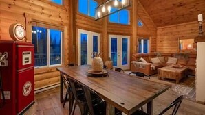 En stuga byggd av timmer med en matplats, ett rött kylskåp och ett stort fönster med utsikt över ett skogsområde.