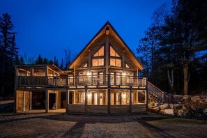 A multi-story wooden cabin with a balcony, set in a forested area.
