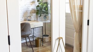 Une pièce avec un plancher en bois, un mur en briques blanches, un bureau avec une chaise, une plante en pot et un luminaire suspendu.