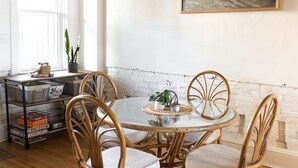 Un coin repas avec une table ronde, quatre chaises en osier, une plante en pot et un tableau accroché au mur.