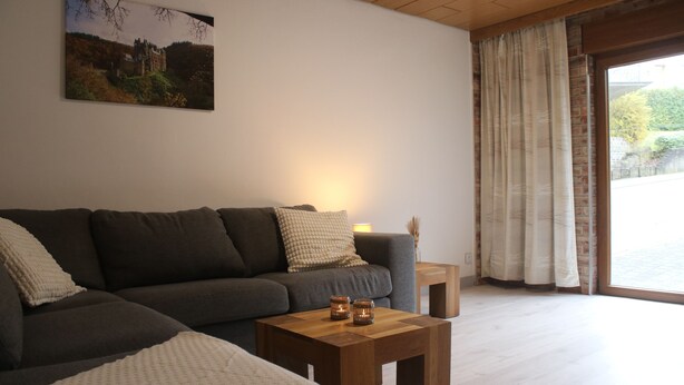 Sala de estar com sofá cinza escuro, mesa de centro de madeira com duas velas e um quadro na parede.