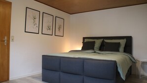 Quarto com cama, porta de madeira e três quadros na parede.