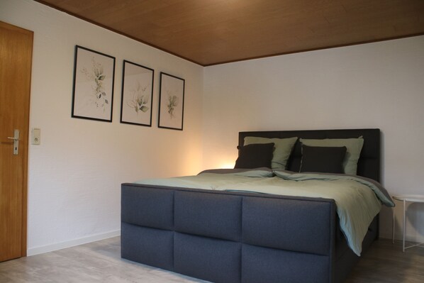 Ein Schlafzimmer mit einem Bett, einer Holztür und drei gerahmten Bildern an der Wand.