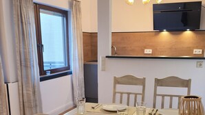 Uma área de refeições com uma mesa posta para quatro pessoas, cadeiras de madeira, uma televisão montada acima da mesa e uma janela com cortinas.