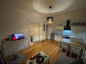 A compact living space with a TV, kitchenette, dining area, and a ceiling light fixture.
