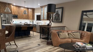 A modern kitchen with wooden cabinets, a dining area with a brown leather couch, and a coffee table with magazines. - Kick back and relaxing luxury home, calm western space near the Broadmoor. (Colorado Springs)