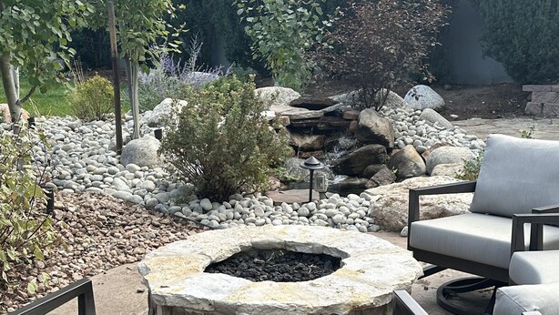 A fire pit surrounded by stone seating and a small waterfall feature in a landscaped garden area. - Kick back and relaxing luxury home, calm western space near the Broadmoor. (Colorado Springs)