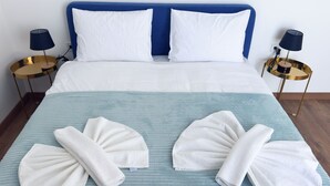 A neatly made bed with white linens, two pillows, and two towels folded on the bed. There are two bedside tables with lamps and a gold-colored base. - Gudauri Ski Resort - Four Seasons (Kazbegi)