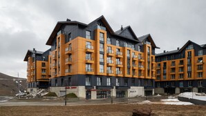 A modern multi-story building with a mix of orange and grey exterior panels, large windows, and balconies. - Gudauri Ski Resort - Four Seasons (Kazbegi)