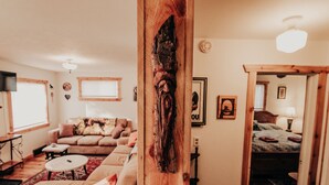 A cozy living room with a large wooden beam, a sofa, a coffee table, and a bed in the background. - Relax in "Big Sky" Style just 3 blocks from the Symes Mineral Soaks! (Hot Springs)