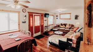 A cozy living room with a wooden floor, a dining table with chairs, a sofa, and a ceiling fan. - Relax in "Big Sky" Style just 3 blocks from the Symes Mineral Soaks! (Hot Springs)