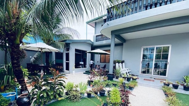 Un edificio moderno con un área exterior cubierta, decorada con diversas plantas en macetas y un pequeño césped.