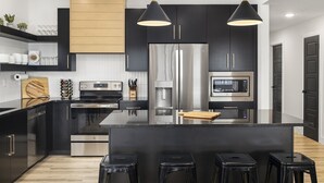 A modern kitchen with black cabinets, stainless steel appliances, and a central island with stools. - New 7 bdrm home (sleeps 28) w/ lake views, sauna, hot tub, & outdoor dining! (HOLLISTER)