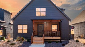 A modern two-story house with a dark exterior, a front porch, and a small deck. - New 7 bdrm home (sleeps 28) w/ lake views, sauna, hot tub, & outdoor dining! (HOLLISTER)