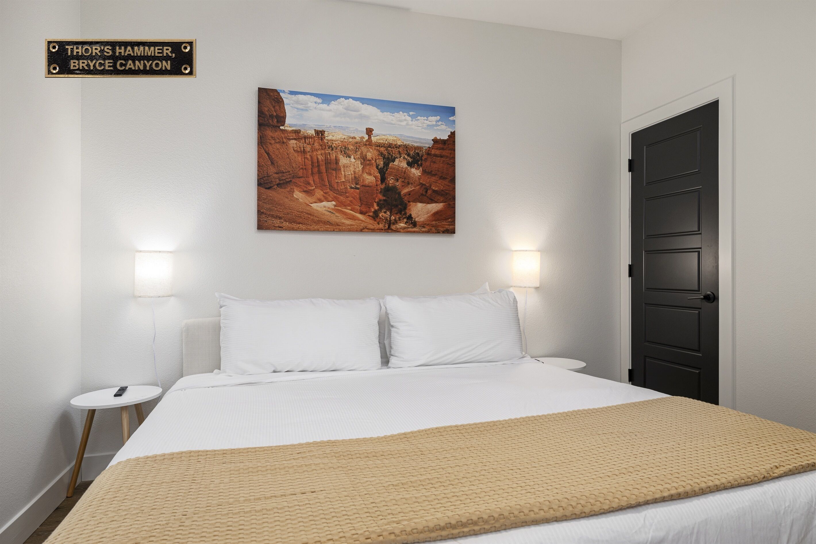 Ein Hotelzimmer mit einem Bett, zwei Nachttischen, einem Bild von Bryce Canyon und einer Tür.