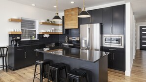 Une cuisine moderne avec des meubles de couleur noire, des appareils en acier inoxydable, un îlot central doté de tabourets de bar et un éclairage suspendu.