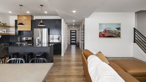 Une cuisine moderne dotée d’un îlot central, d’appareils électroménagers en acier inoxydable et de luminaires suspendus.