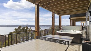 Une terrasse en bois avec un jacuzzi et une table donnant sur un lac.