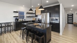 A modern kitchen with a central island, black cabinetry, stainless steel appliances, and pendant lighting.