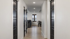 A hallway with a wooden floor, black doors, and a window at the end.