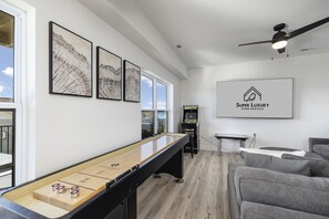 Una sala de estar moderna con una mesa de juego tipo shuffleboard, sofás grises y un ventilador de techo.