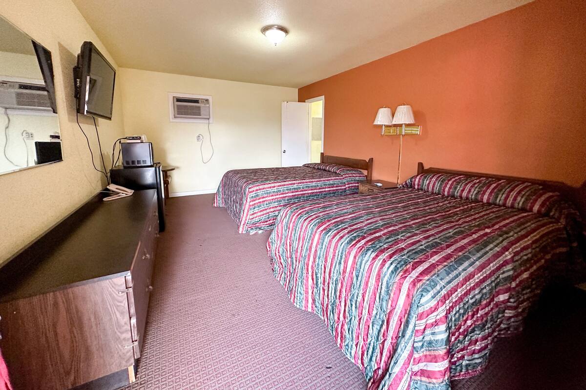 Ein Hotelzimmer mit zwei Betten, einem Schreibtisch, einem Fernseher und einer Lampe.