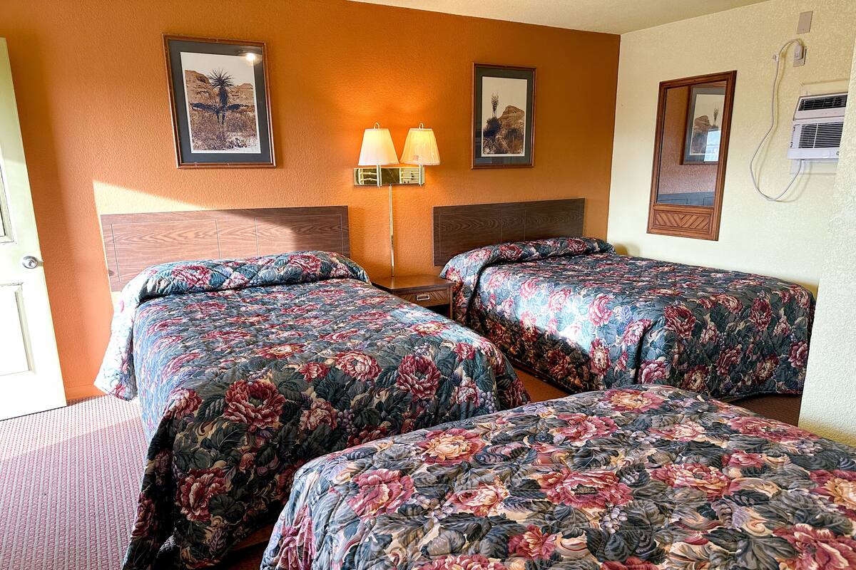 Ein Hotelzimmer mit zwei Betten, einem Nachttisch, einer Wandlampe und gerahmten Bildern an der Wand.