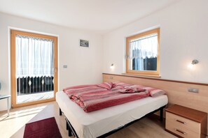A bedroom with a bed, a bedside table, a nightstand, a window, and a door.