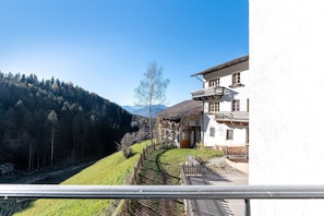 A building with a balcony, a wooden fence, and a view of a forested hillside.