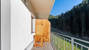 A wooden deck with a railing, a table, and chairs, overlooking a forested area. - Farmhouse 'Innerjerberhof Sunnseit' with Mountain View, Shared Terrace and Wi-Fi (Laurein)
