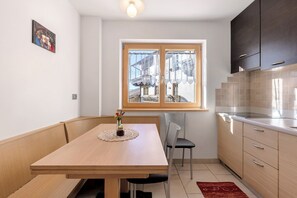 A compact kitchen with a dining table, chairs, a window with curtains, and a view of a building outside.