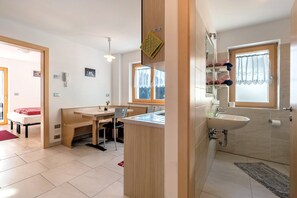 A modern room with a wooden desk, a small kitchen area, a bathroom with a sink and window, and a bed with a red blanket. - Farmhouse 'Innerjerberhof Sunnseit' with Mountain View, Shared Terrace and Wi-Fi (Laurein)