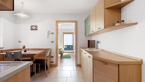 A modern kitchen with wooden cabinets, a dining area with chairs, and a view to a balcony. - Farmhouse 'Innerjerberhof Neiderseit' with Mountain View, Shared Terrace and Wi-Fi (Laurein)