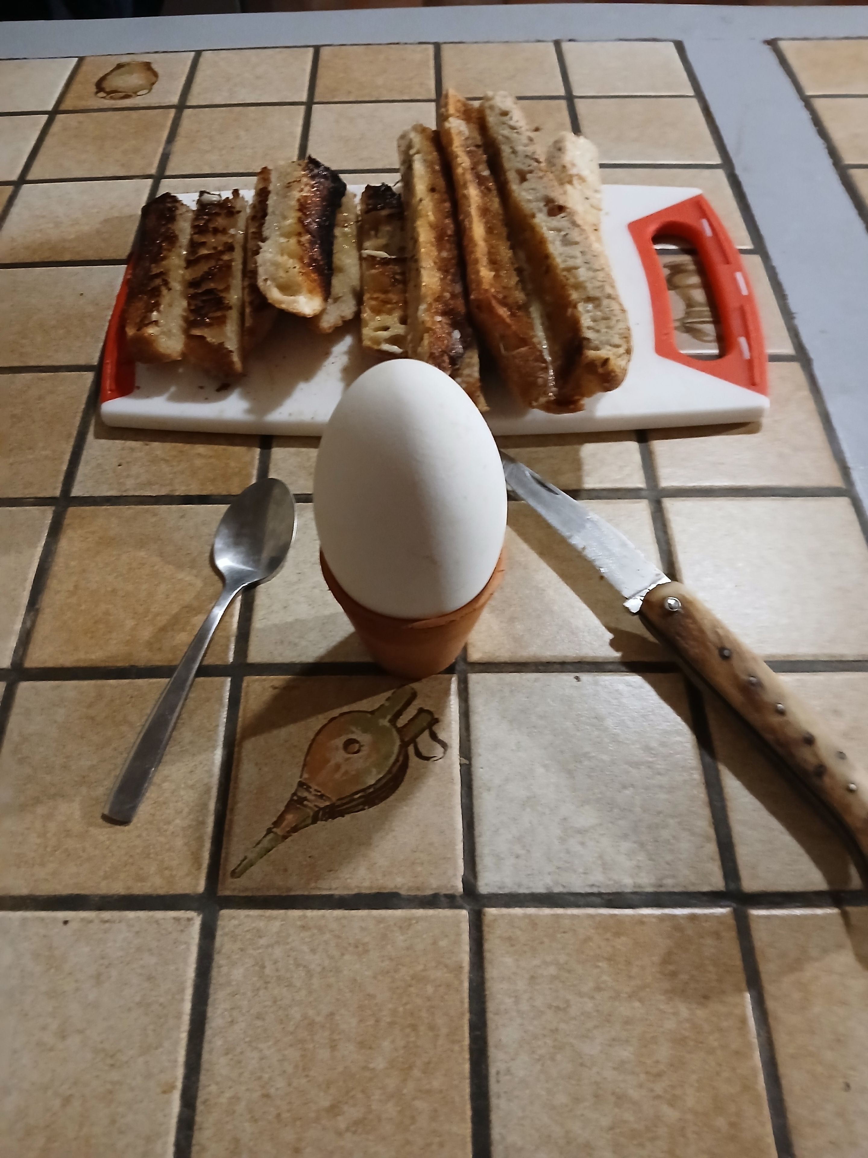 Een keukenblad met een snijplank, een mes, een lepel en een gekookt ei.