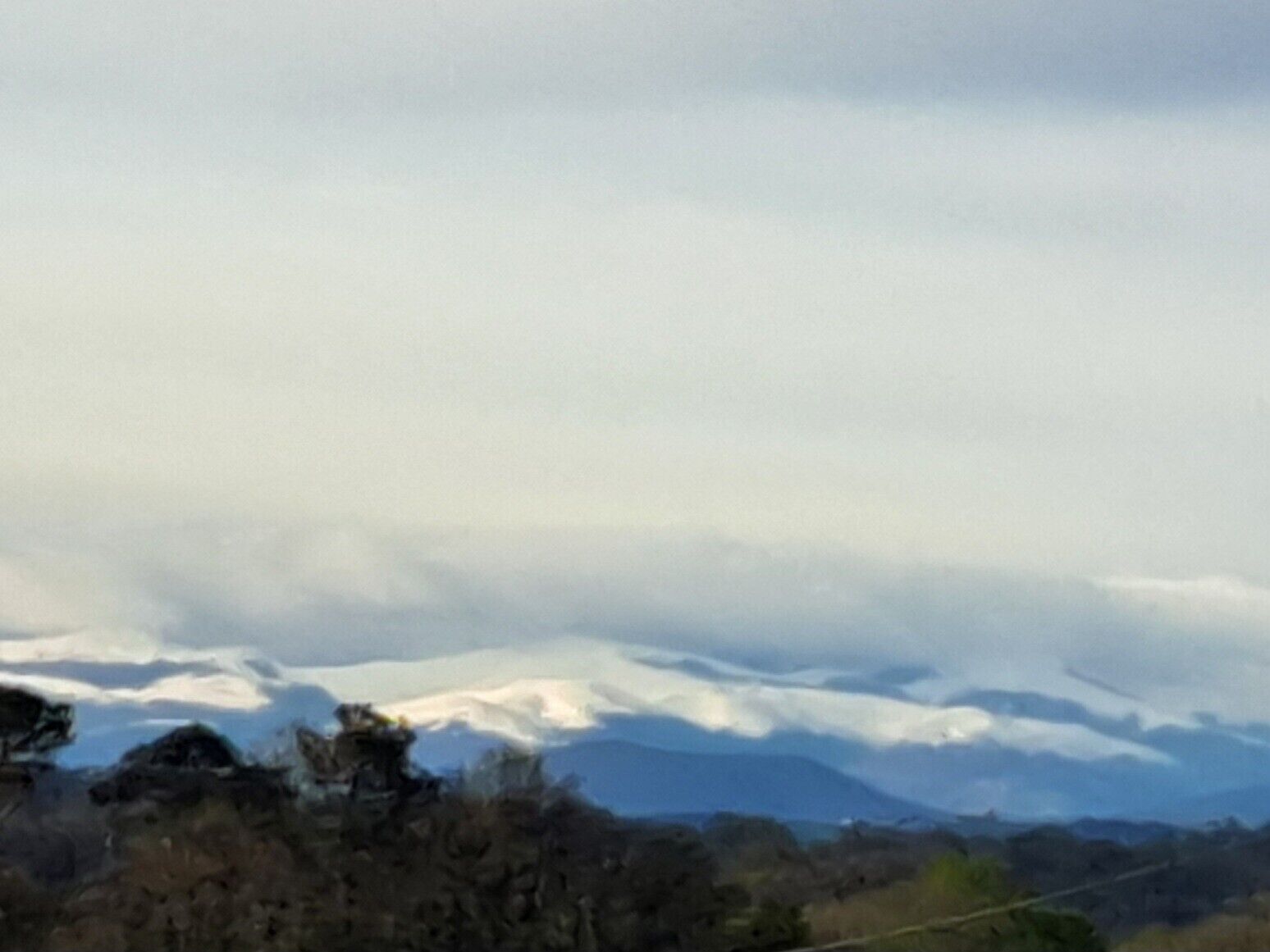 Een bergachtig landschap met besneeuwde toppen en een bewolkte lucht.