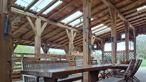 A covered outdoor seating area with wooden benches and tables, a wooden deck, and a view of greenery. - Country House "Domaine Baraque" with Mountain View, Wi-Fi, and Air Conditioning (Pouillon)