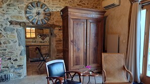 A rustic interior with stone walls, a wooden cabinet, two chairs, a clock, and a kitchen area. - Country House "Domaine Baraque" with Mountain View, Wi-Fi, and Air Conditioning (Pouillon)
