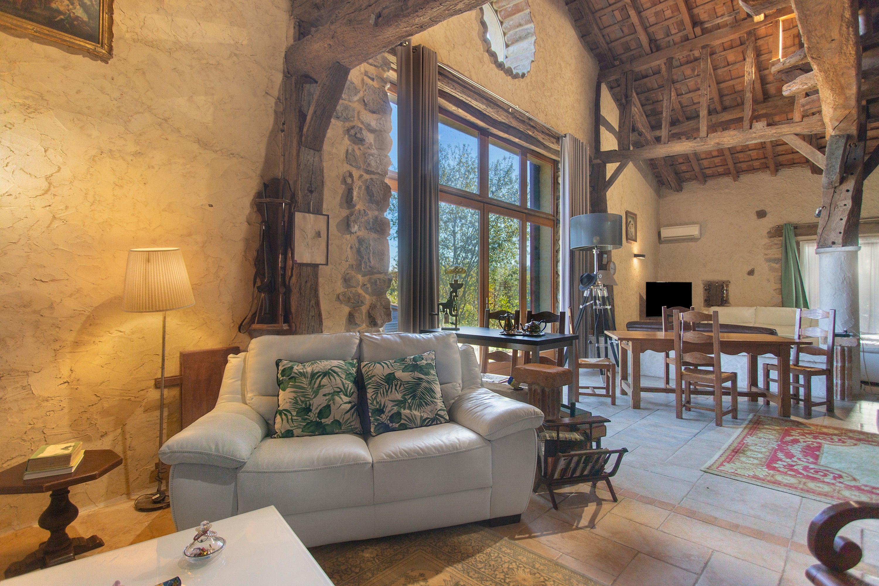 A cozy living room with a stone wall, a sofa, a dining table, and a kitchen area.
