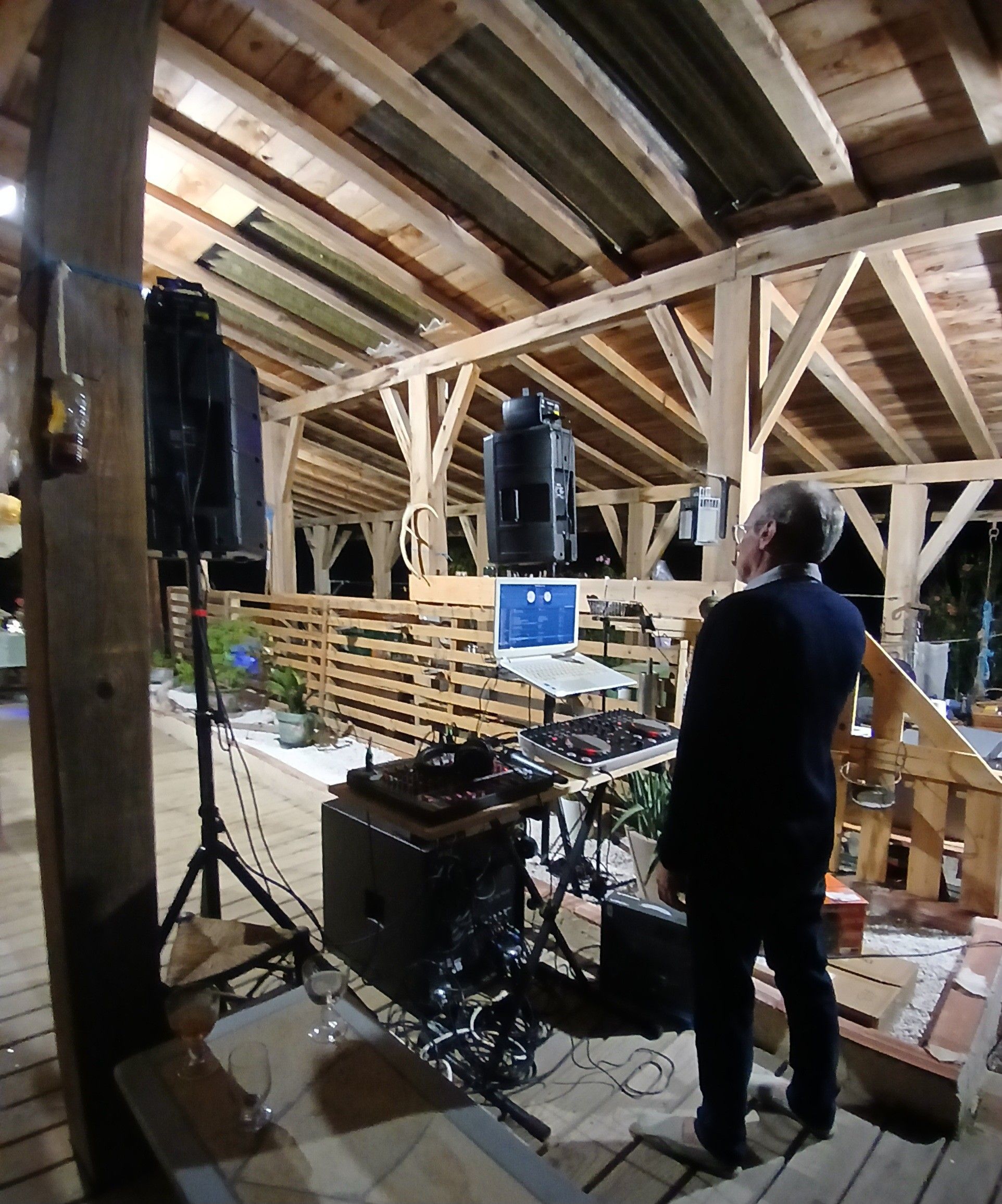 Ein Innenraum mit Holzbalkendecke, einer DJ-Anlage und einem Laptop auf einem Tisch.