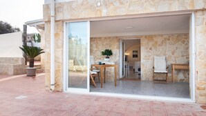 Esterno in pietra con una porta vetrata che dà su un interno con zona pranzo, una sedia e un tavolo.