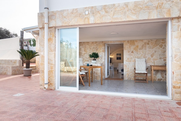 Une façade en pierre avec une porte en verre donnant sur un intérieur comprenant un coin repas, une chaise et une table.