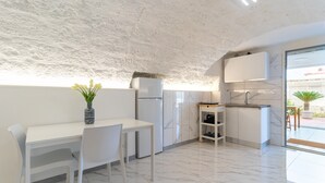 Una cucina moderna con mobili bianchi, una parete protettiva in marmo e un'area pranzo con tavolo e sedie bianche.