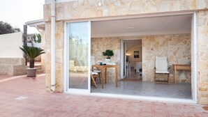 A stone exterior with a glass door leading to an interior with a dining area, a chair, and a small table.