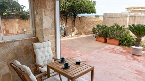 Ein Zimmer mit Stehwänden, einem Holztisch und -stühlen, einer Topfpflanze und Blick auf das Meer.