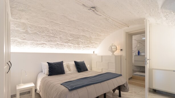 Ein Schlafzimmer mit Bett, Nachttisch, Lampe und Blick ins Bad.